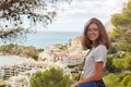Young Caucasian happy girl stands on a hill and looks at us, against the background of the Mediterranean coast and Royalty Free Stock Photo