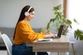 Young Caucasian lady in headphones using laptop pc, working online from home, copy space Royalty Free Stock Photo