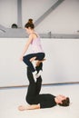 A young Caucasian male and female couple practicing acrobatic yoga in a white gym on mats. They are in a pose REVERSE THRONE. Royalty Free Stock Photo