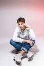 Young caucasian male model posing while sitting on the floor in the studio. Teenage boy in stylish clothes on a pink background. Royalty Free Stock Photo