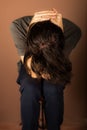 Young Caucasian male seated in a chair with their head resting in their hands, appearing thoughtful