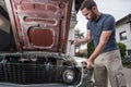 Young caucasian male is seen wrenching an engine or engine bay of an old vintage car. Tune up or checkup of a vintage car