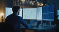 Young caucasian male software developer analyzing code on multiple monitors in office