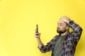 A young caucasian man with a beard and a bald head holding a phone in his hands on a yellow background. Guy holds his head by head Royalty Free Stock Photo