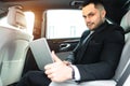 Confident businessman holding laptop on legs while sitting in executive car Royalty Free Stock Photo