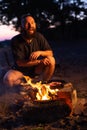 A young man with a beard prepares a dish of bacon with scrambled eggs on a fire. Cooking and outdoor recreation in