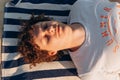 Young Caucasian man with curly hair, closed eyes, resting, relaxing or sleeping in white T-shirt with word Summer lies on striped