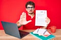 Young caucasian man with curly hair sitting on the table showing failed exam with open hand doing stop sign with serious and Royalty Free Stock Photo