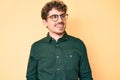 Young caucasian man with curly hair wearing casual clothes and glasses looking away to side with smile on face, natural expression Royalty Free Stock Photo