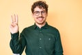 Young caucasian man with curly hair wearing casual clothes and glasses showing and pointing up with fingers number three while Royalty Free Stock Photo