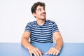 Young caucasian man with curly hair wearing casual clothes sitting on the table looking away to side with smile on face, natural Royalty Free Stock Photo