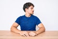 Young caucasian man with curly hair wearing casual clothes sitting on the table looking to side, relax profile pose with natural Royalty Free Stock Photo