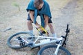 Young caucasian man with dark hair saws the bicycle laying on the ground in abandoned park with big blue and yellow hand saw. Fun,