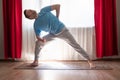 Young caucasian man doing yoga utthita parshvokonasana pose at his living room