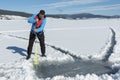 Young Caucasian man drilling the ice on a frozen lake with ice auger drill. Selective focus