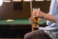 Young Caucasian man drinks beer while sitting on a billiard table, player resting after a game of billiards Royalty Free Stock Photo