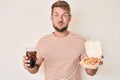 Young caucasian man eating fast food puffing cheeks with funny face