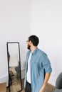 Young caucasian man in glasses standing at the mirror in living room