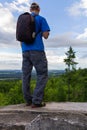 Young caucasian man, hiker in cap with backpack from back standing on rock and looking to valey. Czech summer landscape Royalty Free Stock Photo