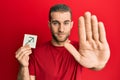 Young caucasian man holding paper with sagittarius zodiac sign with open hand doing stop sign with serious and confident