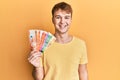 Young caucasian man holding philippine peso banknotes looking positive and happy standing and smiling with a confident smile Royalty Free Stock Photo