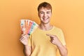 Young caucasian man holding philippine peso banknotes smiling happy pointing with hand and finger Royalty Free Stock Photo