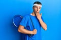 Young caucasian man holding tennis bag covering mouth with hand, shocked and afraid for mistake