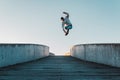 Young caucasian man in jeans and hoodie jumping on concrete bridge. Mid air parkour pose in city environment and clear sky