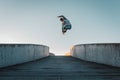 Young caucasian man in jeans and hoodie jumping on concrete bridge. Mid air parkour pose in city environment and clear sky