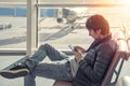 Young caucasian man in jeans and jacket sitting in airport waiting lounge hall, using mobile phone. Royalty Free Stock Photo