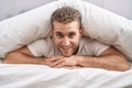 Young caucasian man lying on bed covering with bedsheet at bedroom