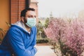 Young caucasian man with mask looking out onto home terrace during quarantine due to coronavirus covid19 pandemic Royalty Free Stock Photo