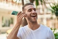 Young caucasian man miling confident listening audio message by the smartphone at street