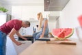 Young caucasian man opening dishwasher, while his girlfriend who is sitting on kitchen counter, holds glass of red wine Royalty Free Stock Photo