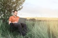 Young caucasian man in orange shirt working on his laptop sitting on a camping chair in meadow. Royalty Free Stock Photo