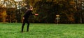 Young caucasian man playing disc golf on autumn play course with basket Royalty Free Stock Photo