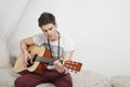 Young Caucasian man playing guitar while sitting on fur sofa Royalty Free Stock Photo