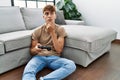 Young caucasian man playing video game holding controller at home serious face thinking about question with hand on chin, Royalty Free Stock Photo