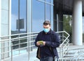 A young Caucasian man in a protective mask and black glasses stands near a car, bought a new green protective mask for a woman.