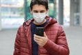 Young caucasian man with protective mask reading news or message on smartphone in modern city street Royalty Free Stock Photo