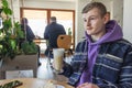 Young caucasian man in purple sweater having coffee break in the cafe. Drinking latte with cheesecake.