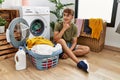 Young caucasian man putting dirty laundry into washing machine looking confident at the camera smiling with crossed arms and hand Royalty Free Stock Photo