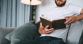 Young caucasian man resting on a sofa and reading a book. Home leisure Royalty Free Stock Photo