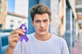 Young caucasian man with serious expresison holding purple ribbon at the city Royalty Free Stock Photo