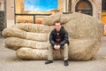 Young caucasian man sitting on huge stone hand on street of Antwerp, Belgium in early spring day. Antwerpen travel tourism