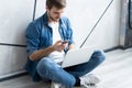 Young caucasian man sitting over gray wall using computer laptop and smartphone. Royalty Free Stock Photo