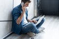 Young caucasian man sitting over gray wall using computer laptop and smartphone. Royalty Free Stock Photo