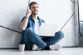 Young caucasian man sitting over gray wall using computer laptop and smartphone. Royalty Free Stock Photo