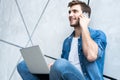 Young caucasian man sitting over gray wall using computer laptop and smartphone. Royalty Free Stock Photo