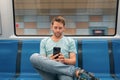 Young Caucasian man sitting in the train on the subway and using mobile phone. Male traveler in metro train surfing Royalty Free Stock Photo